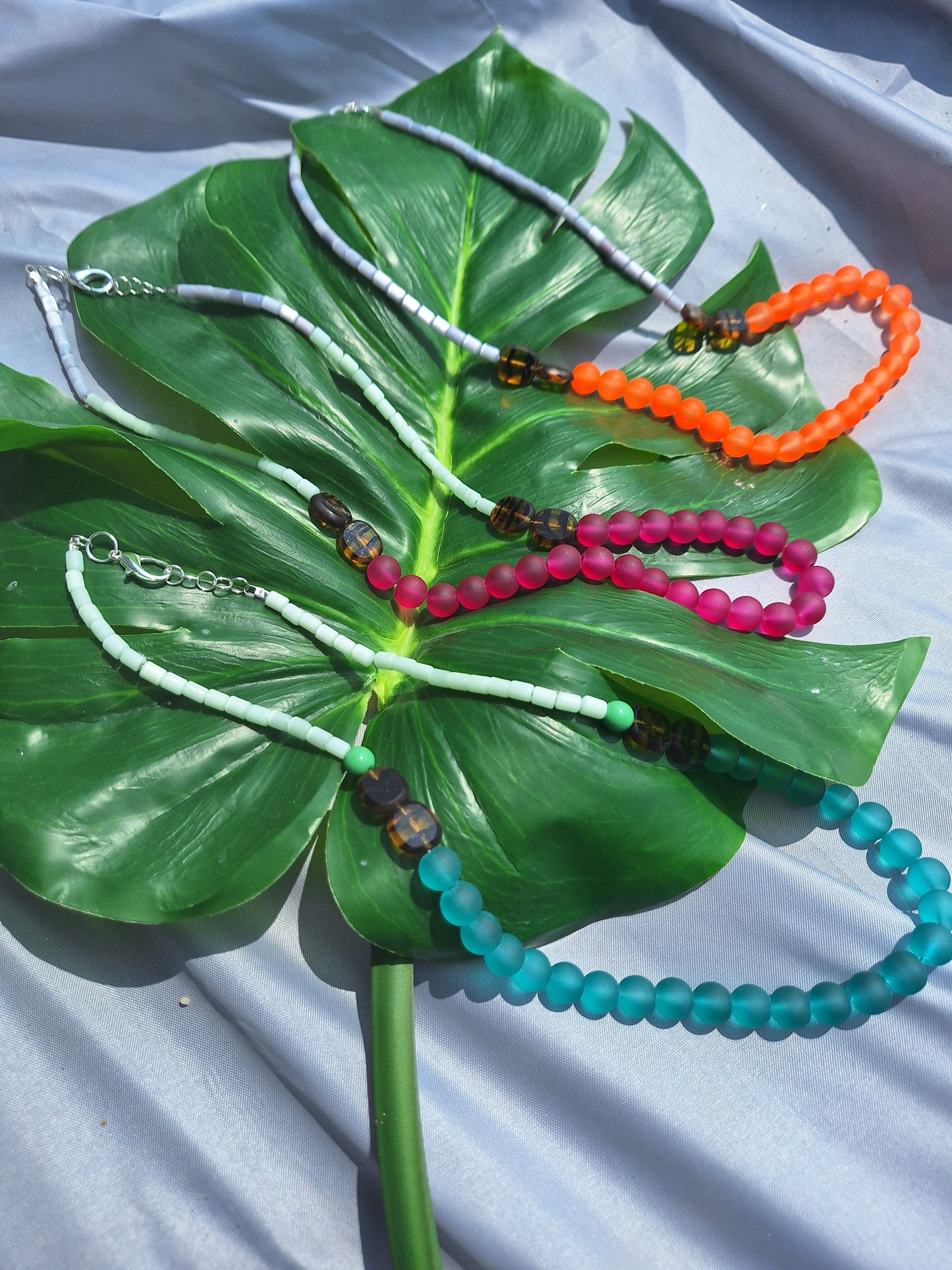 Colorful beaded necklaces on a large green leaf with a white background