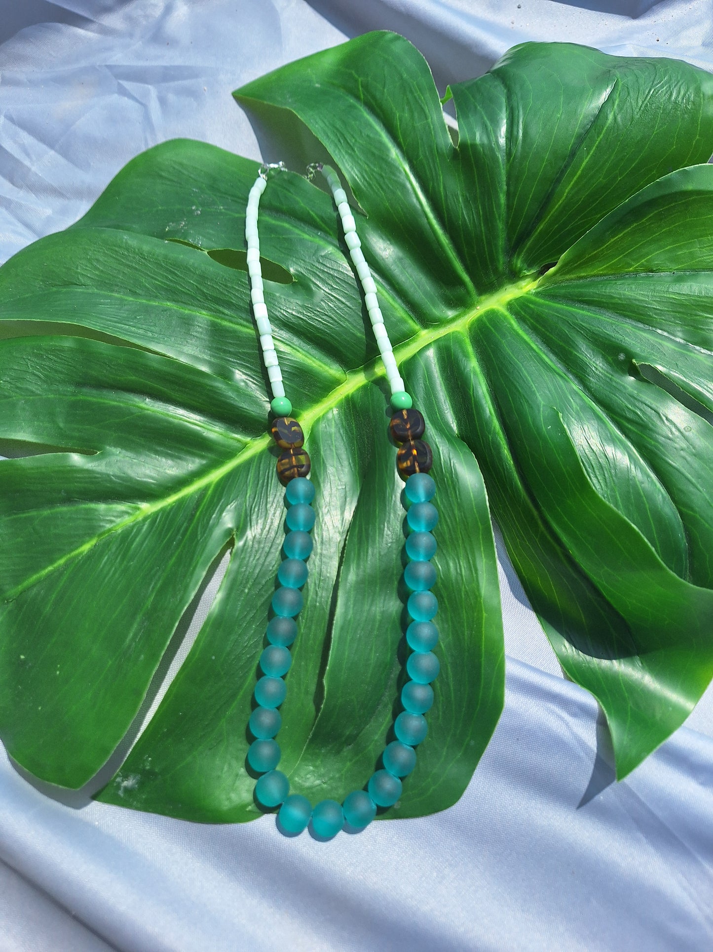 Two beaded necklace on a large green leaf with a light blue necklace