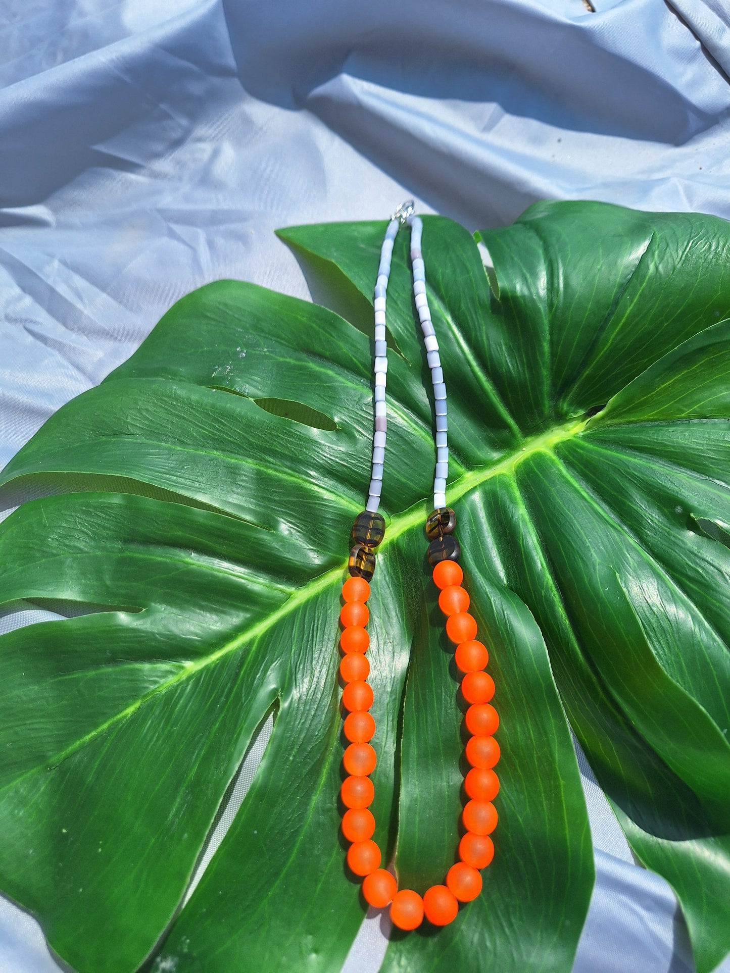 Two beaded necklace on a large green leaf with a light blue fabric background